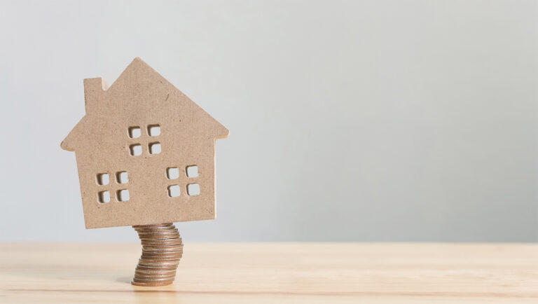 house sitting precariously atop stack of coins - real estate myths for home sellers concept