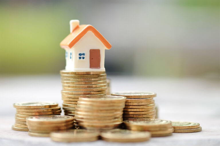Model house atop gold coins, representing home affordability and pricing trends.