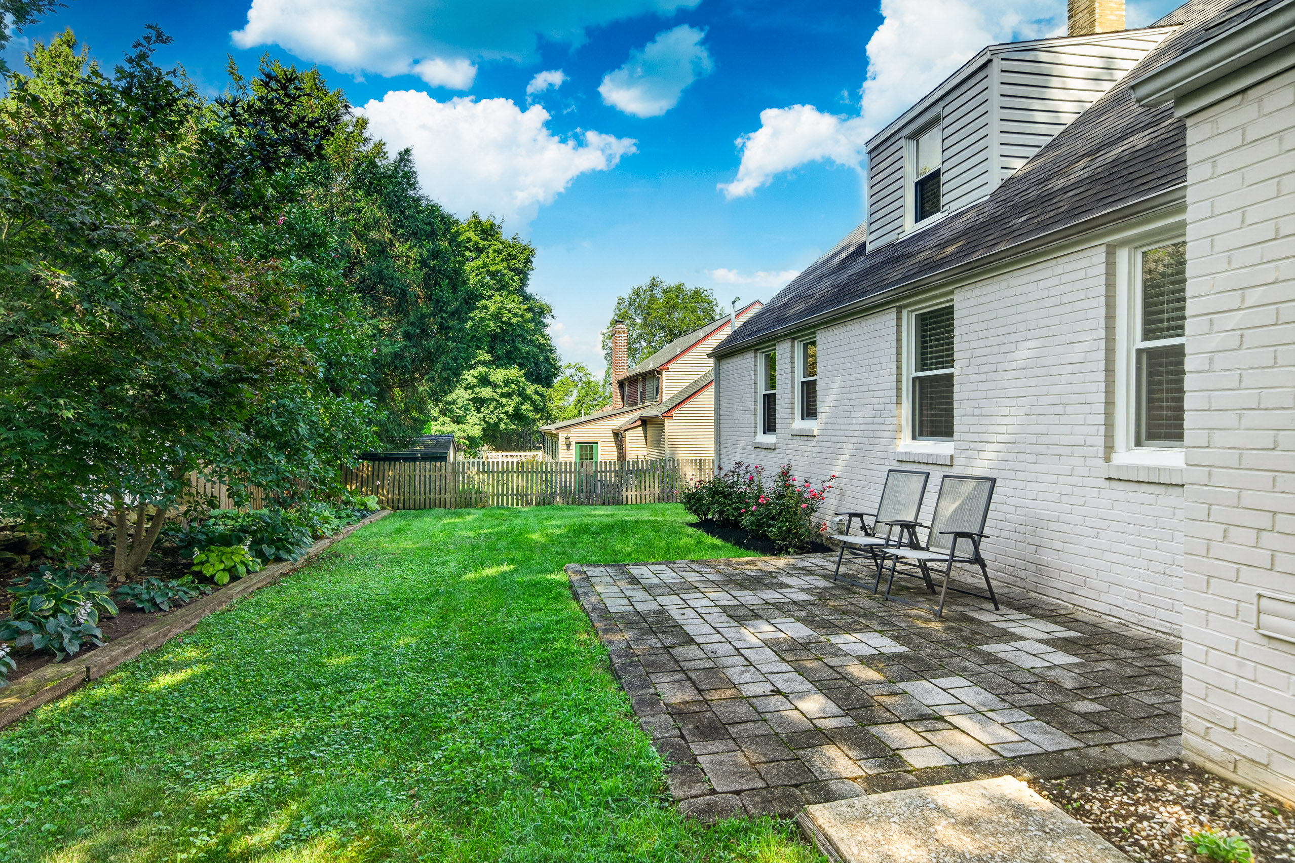 Fenced backyard with stone patio, mature landscaping, and seating area