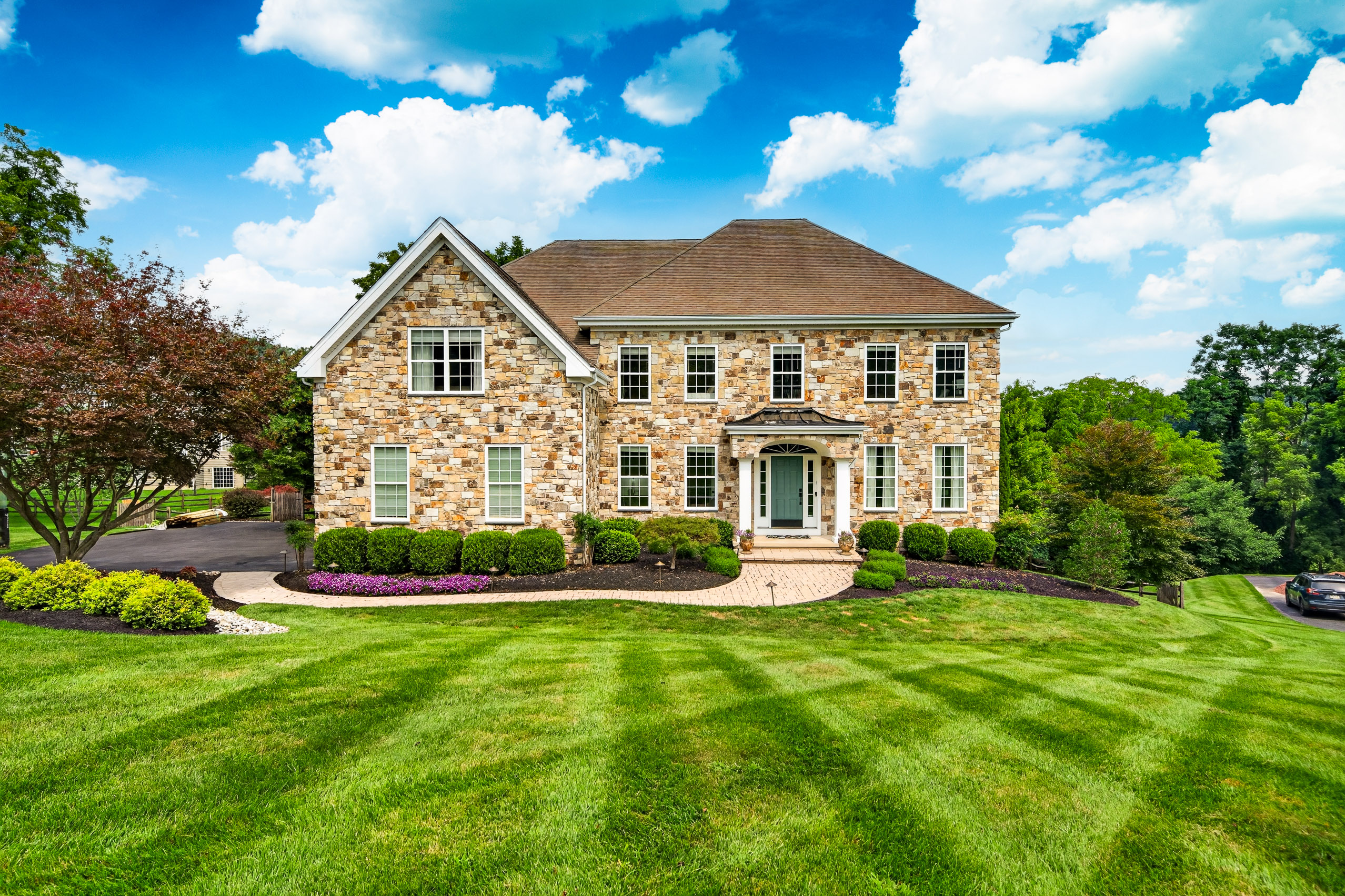 Stone colonial front exterior with two-story stacked-stone facade, arched entry portico, and manicured lawn