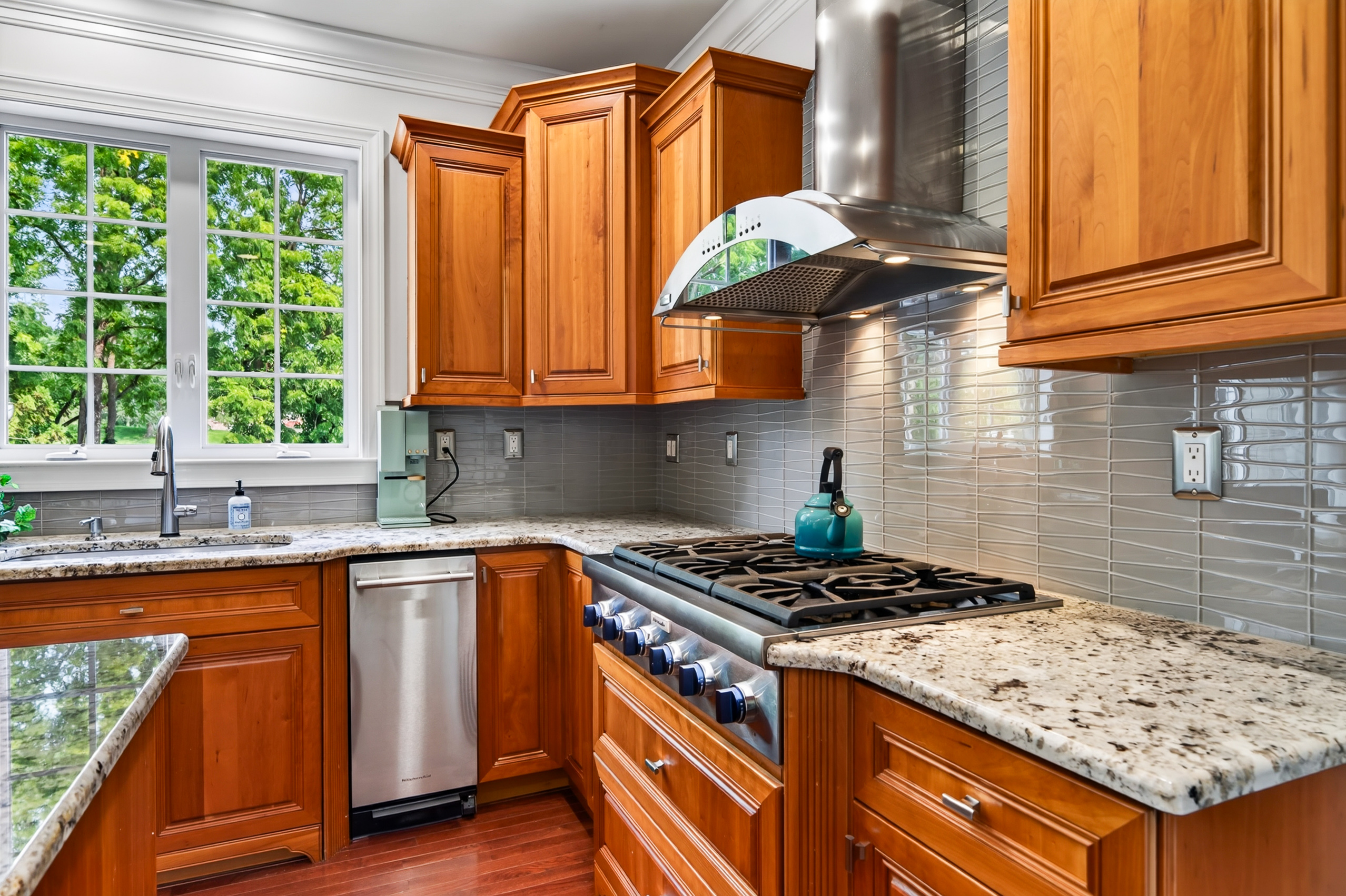 Kitchen with granite countertops, six-burner gas range, and stainless range hood over tile backsplash