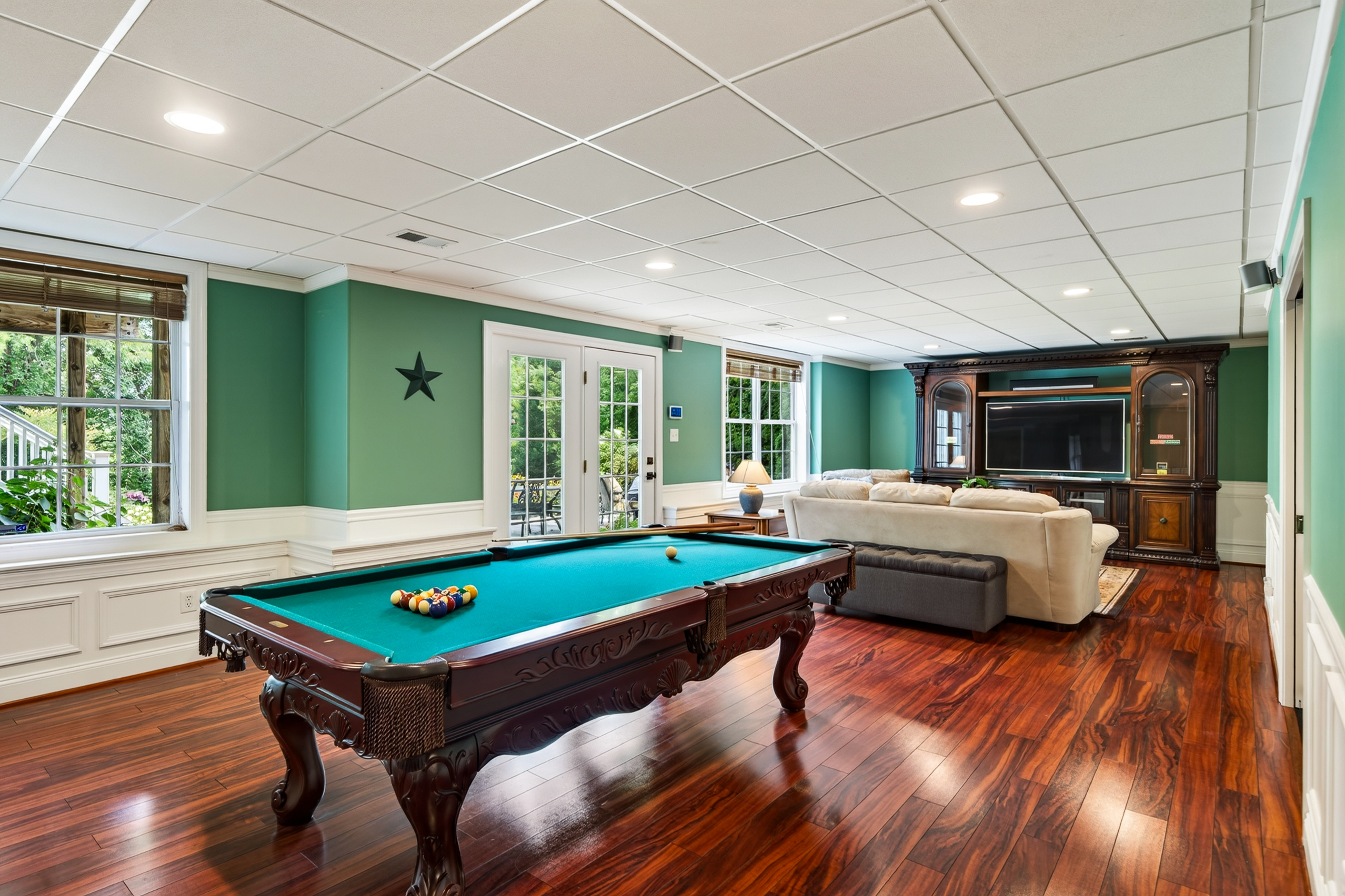 Finished lower level with pool table, wood flooring, and walk-out French doors to the patio