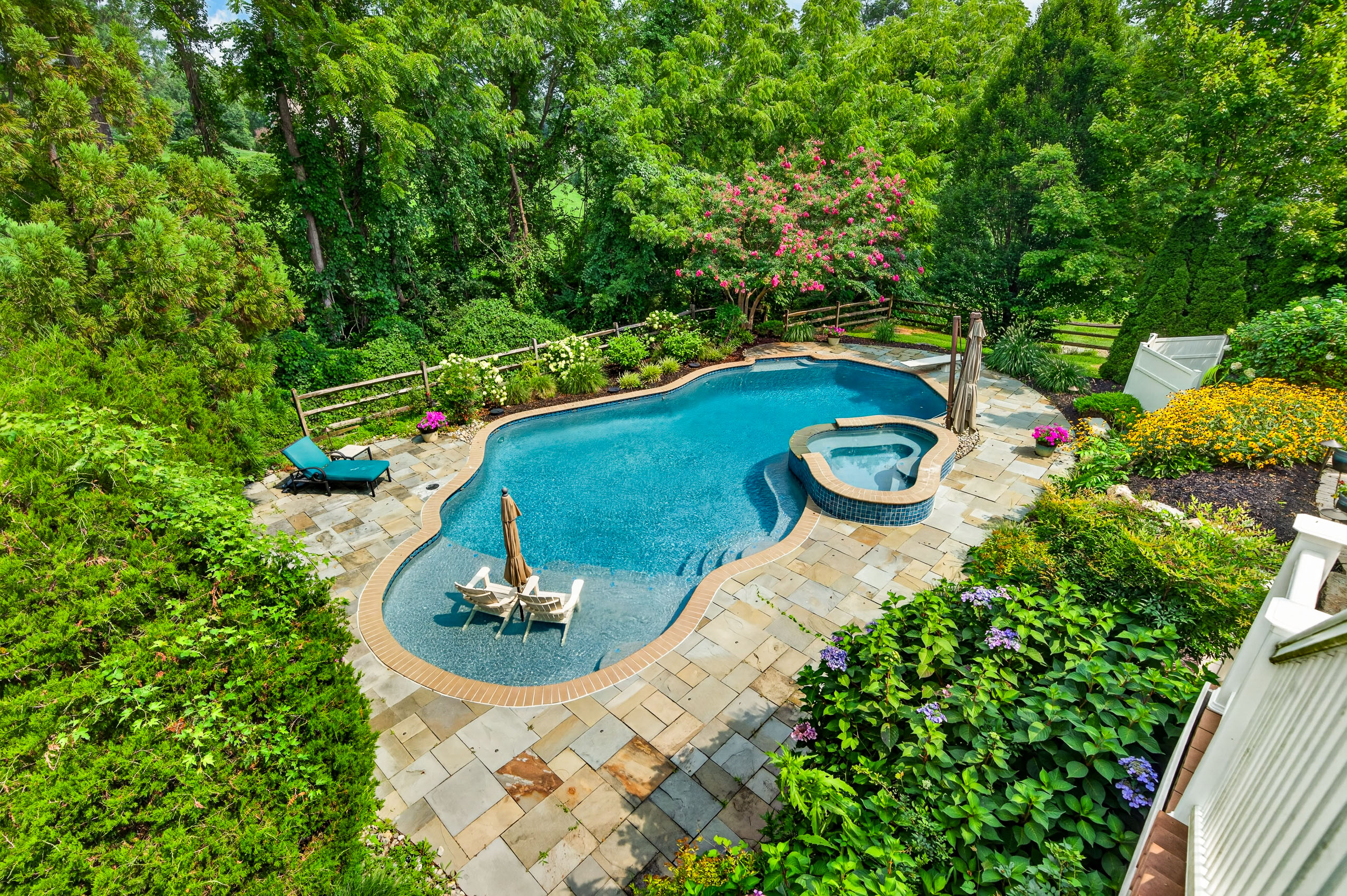 Saltwater pool with beach entry, attached spa, and stone patio surrounded by mature landscaping